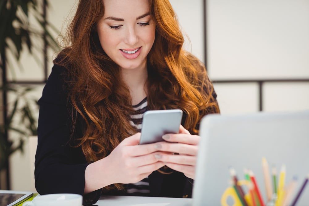 Happy beautiful young woman using cellphone at creative office