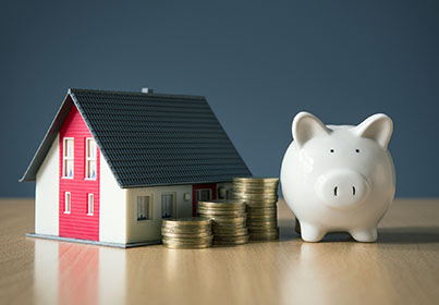 tiny house next to a piggy bank with stacks of coins in the middle